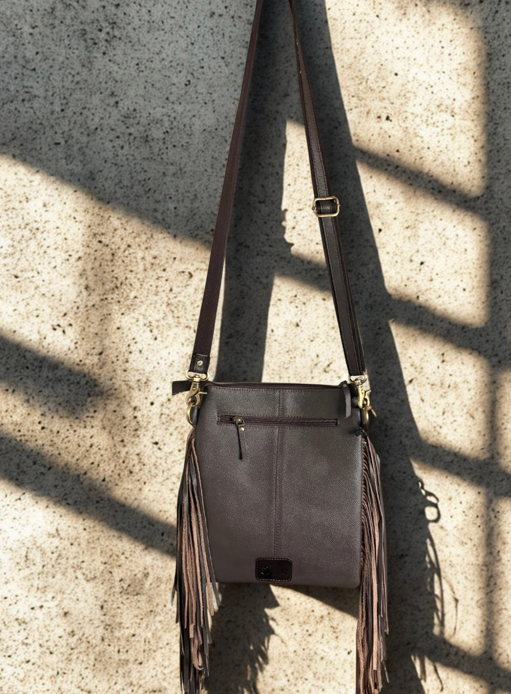 Brown leather crossbody bag with fringe details on a textured concrete surface genuine Leather